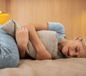 Pregnant woman lying on sofa holding her abdomen, showing discomfort or pain.