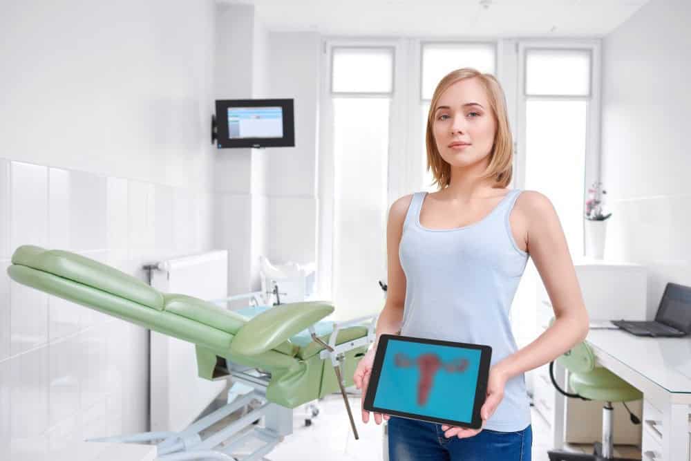 Woman holding tablet with uterus diagram in gynecology clinic.